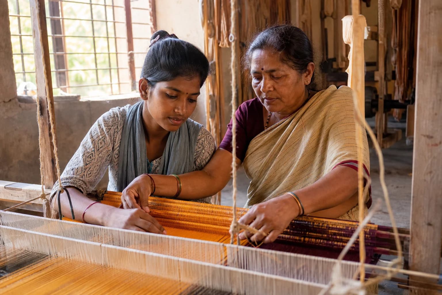 Skill Development — a young apprentice learning traditional handloom weaving from a master craftswoman